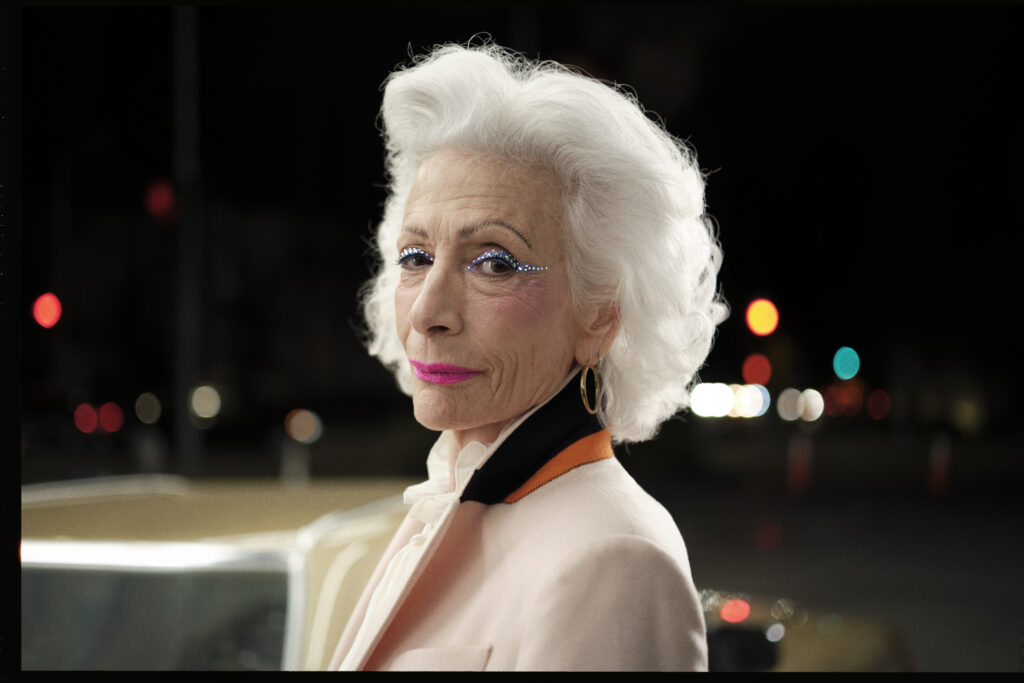 A campaign image from Half Magic Beauty of an older model with white hair wearing blue eyeshadow and pink lipstick
