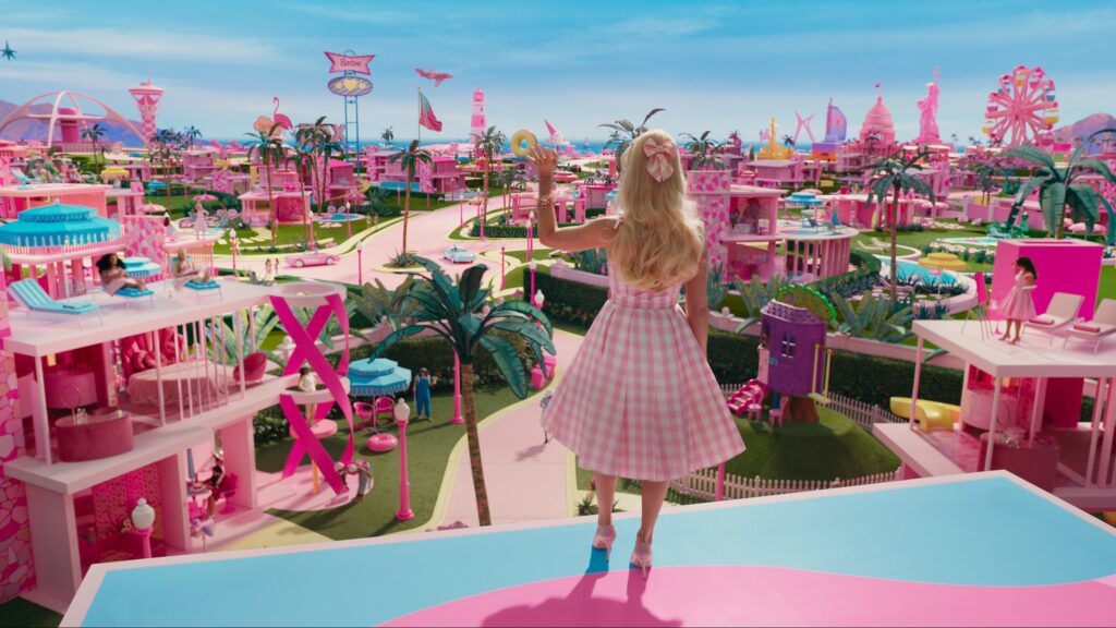 A still from the Barbie Movie that shows Margot Robbie as Barbie looking over a pink and blue Barbie town